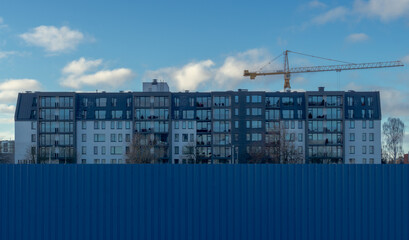 Fototapeta na wymiar Blue metal fence. modern multi-storey house. yellow construction crane.