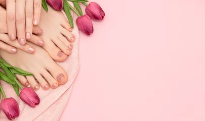 Fotobehang Vrouwelijke handen met veernagelontwerp. Glitter roze nagellak pedicure. Vrouwelijke handen en voeten met tulp bloemen op roze achtergrond. Ruimte kopiëren. © devmarya