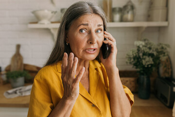 Attarctive retired female gesticulating with anxiety talking on phone, having worried face, using smartphone for conversation wih bank, trying to solve problem with savings account