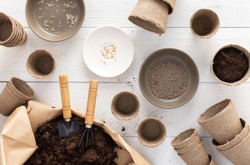 Eco friendly pots for seedlings on a white wooden background, small bag with ground and garden trowel with rake, planting seeds in disposable peat pots
