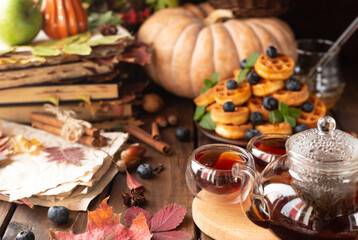 many waffles are stacked on a plate, decorated with mint leaves and blueberries. Tea in a glass teapot and two small bowls