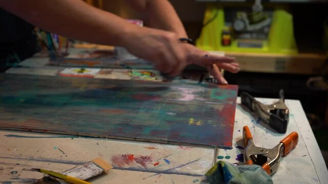Artist scraping painted canvas in his home studio