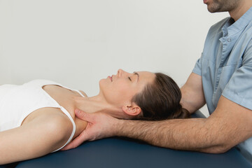 Female patient receiving osteopathic neck and shoulder treatment. Therapist manipulating back of...