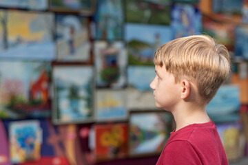 A boy in an art gallery looks at the paintings in the exhibition hall with attention.