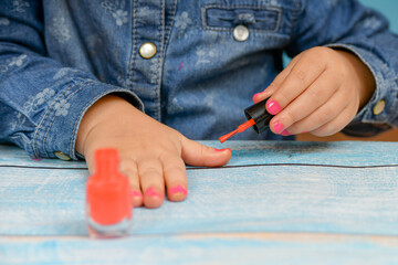 Little girl paints her nails with her mother's nail polish.