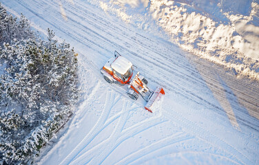Fototapeta na wymiar Snow removing with red tractor on the road. Suny winter day, Drone top view.
