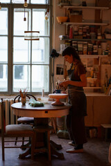 Young woman potter maker work with clay on pottery wheel in creative art space, professional studio. Female artist creating handicraft ceramics for hobby. Relax at handcraft products workshop concept