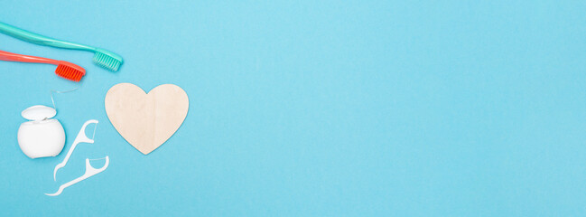 Banner with accessories for oral care on a blue background. Wooden heart. Dental hygiene. Copy space. Place for text and logo. Toothbrush and dental floss. Flat lay. Concept