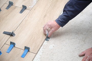 Contractor hands laying ceramic wood effect tiles using tile levelers.