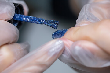 a close-up manicure master applies a thick layer of blue gel polish to the client's nail
