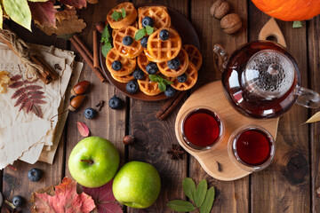 many waffles are stacked on a plate, decorated with mint leaves and blueberries. Tea in a glass teapot and two small bowls