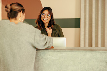 Smiling receptionist assisting a woman with signing in to an office - obrazy, fototapety, plakaty