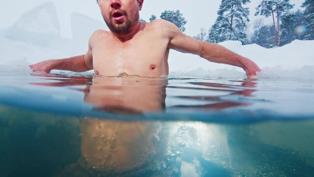 Winter swim. Young man swims in the winter lake. Splitted above and under view of the man swimming in the icy water