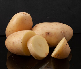 Patatas crudas enteras y cortadas  sobre fondo negro. Whole and sliced ​​raw potatoes on black...