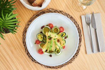 From above fresh zucchini rolls served in bowl with avocado slices and halves of cherry tomatoes in restaurant