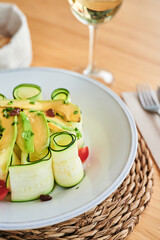 Vertical high angle of fresh zucchini rolls served in bowl with avocado slices and halves of cherry tomatoes in restaurant