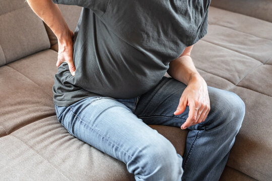 Mann &uuml;ber 50 mit Schmerzen im unteren R&uuml;cken sitzt auf einer beigen Couch.