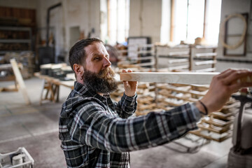 Mature male carpenter carrying wooden board indoors in carpentery workshop. Small business concept.