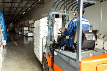 A man on a forklift works in a large warehouse, unloads bags of raw materials