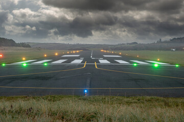 Small illuminated runway of a small airport. Dark dramatic cloudy sky. Aviation industry. Nobody....