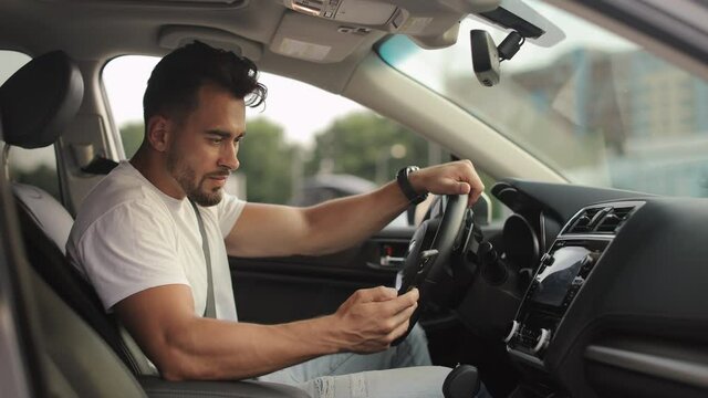 A man is sitting in the driver's seat. He is texting on his smartphone. He is smiling. Shooting from the side seats. 4K 50fps