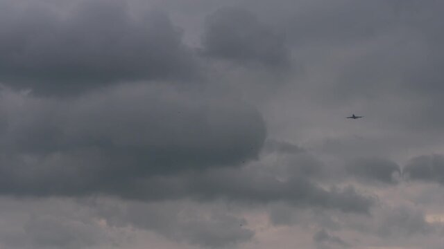 looking up at a Boing 747 passenger jet plane in the distance, flying through dark clouds in sky.