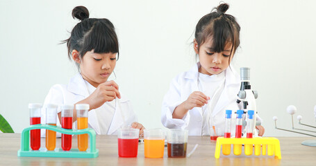 Little girl asian cute little student child learning research and doing a chemical experiment while making analyzing and mixing liquid in test tube at home on the table.