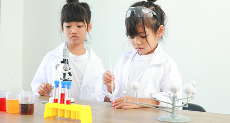 Little girl asian cute little student child learning research and doing a chemical experiment while making analyzing and mixing liquid in test tube at home on the table.