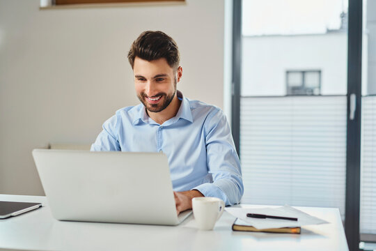 Smiling young businessman working on laptop