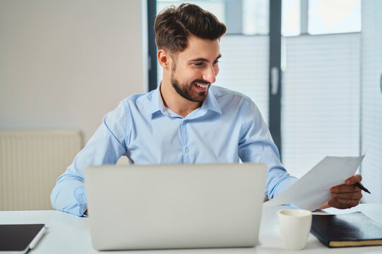 Happy young man working at office looking on document