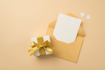 Top view photo of open pastel yellow envelope with paper sheet white hearts and white giftbox with gold ribbon bow on isolated beige background with empty space