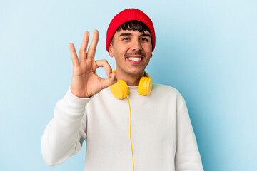 Young mixed race man listening to music isolated on blue background cheerful and confident showing ok gesture.