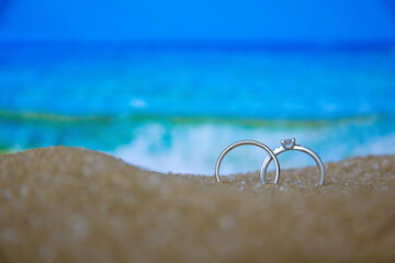 Two wedding silver rings in the sand on the background of beach and sea.