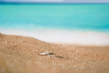 Two wedding white gold rings in the sand on the background of beach and sea.
