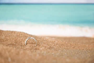 Make an offer on the seashore. Diamond engagement ring in sand on the background of water and ocean waves.