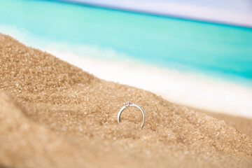 Make an offer on the seashore. Diamond engagement ring in sand on the background of water and ocean waves.
