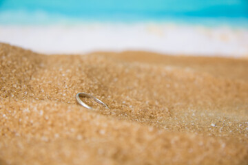 Fototapeta na wymiar One engagement silver ring in the sand on the background of beach and sea.