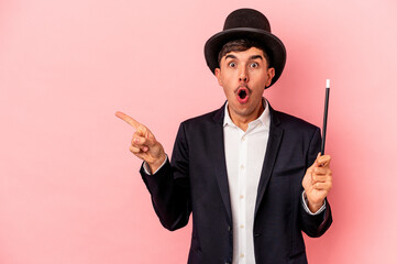 Young caucasian wizard man holding a wand isolated on pink background pointing to the side