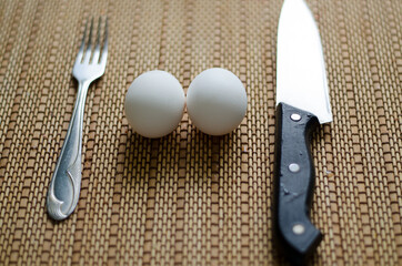 still life, kitchen, two white eggs, a kitchen knife and fork lie on a bamboo mat