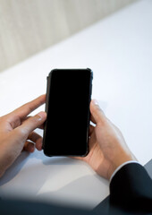 Businessman in black suit holding blank screen mobile phone with both hand.
