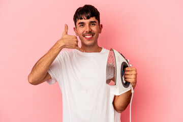 Young mixed race man holding an iron isolated on pink background showing a mobile phone call gesture with fingers.