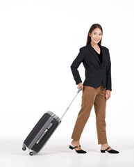 Young asian women in black suit smiles as she walks dragging a black suitcase. Portrait on white background with studio light.