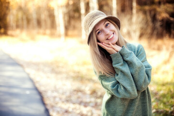 Young beautiful girl in a hat and green dress enjoys a walk in the park