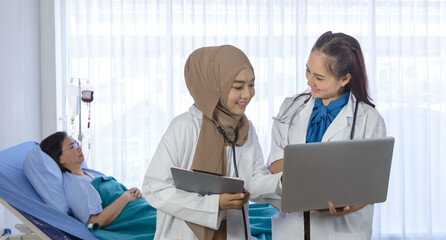 muslim doctor and female doctor using laptop computer and discussion about examining medical report of elderly patient while standing in font of elderly patient lie down on bed in the hospital room.