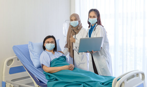 Muslim female doctor using stethoscope checking pressure and young asian female doctor hold laptop and giving advice discussion to elderly patient lie down on bed at hospital. Medicine and health care