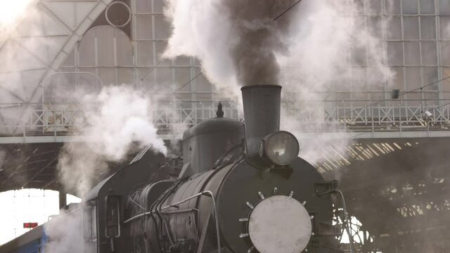 Retro steam train departs from the railway station. Old black steam train with blue cars