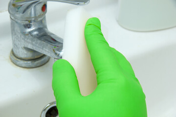 Cleaning plumbing and bathroom. A gloved hand rubs the tap with a melamine sponge.