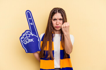Young sports fan woman isolated on yellow background showing fist to camera, aggressive facial expression.