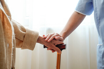 Senior woman holding quad cane handle in elderly care facility. Hospital nurse comforting mature...