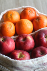Two sustainable shopping bags filled with apples and oranges on wooden table. Selective focus.